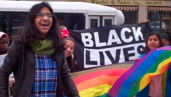 Student speaks at rally with pride flag and Black Lives Matter banner